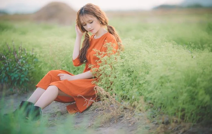 Cô gái mặc váy cam ngồi trên cỏ làm hình nền