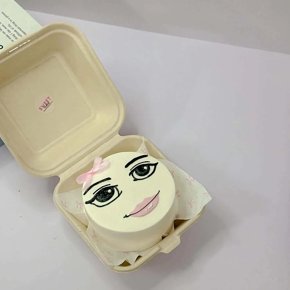 Bánh sinh nhật hài hước vẽ gương mặt cô gái với đôi mắt và môi hồng trong hộp bento